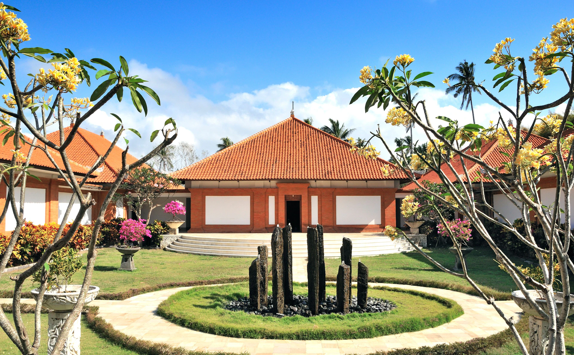 A building with a red-tiled roof and white walls, surrounded by manicured gardens and flowering trees.