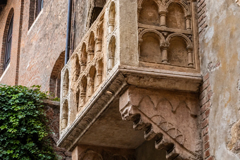 A detailed view of a historic stone balcony with intricate arch designs and carvings, attached to a brick building.