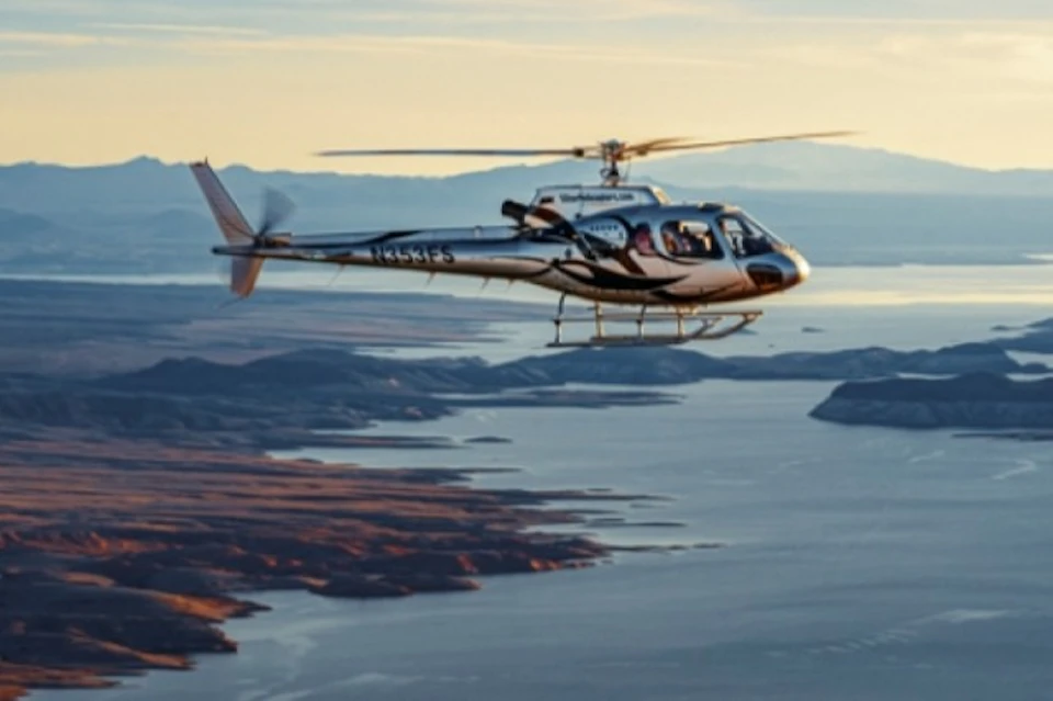 A helicopter in flight over a scenic landscape with water, land, and distant mountains during sunset or sunrise.