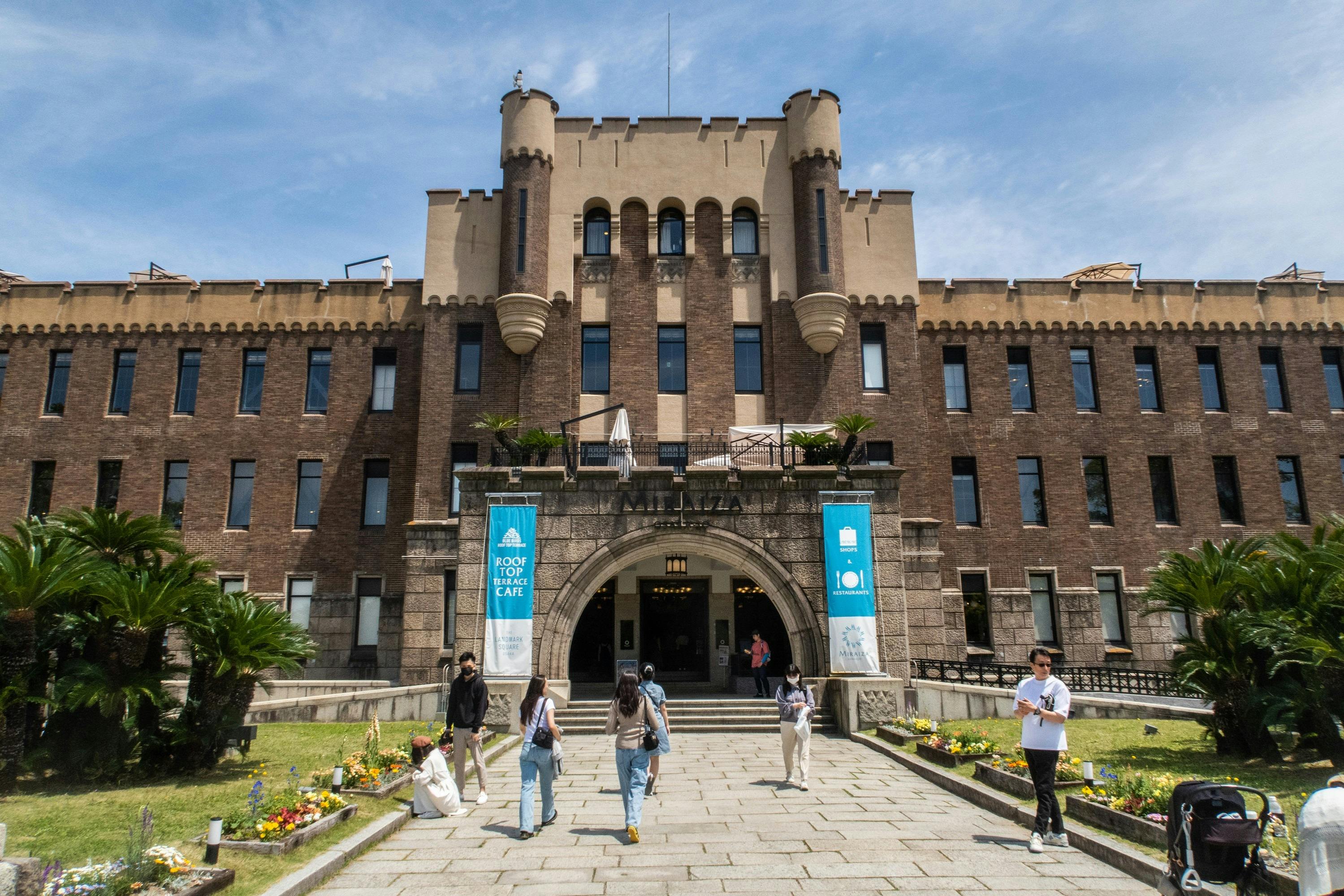 人们走在一栋历史悠久的大型砖砌建筑前，该建筑设有中央拱形入口、横幅和修剪整齐的草坪。