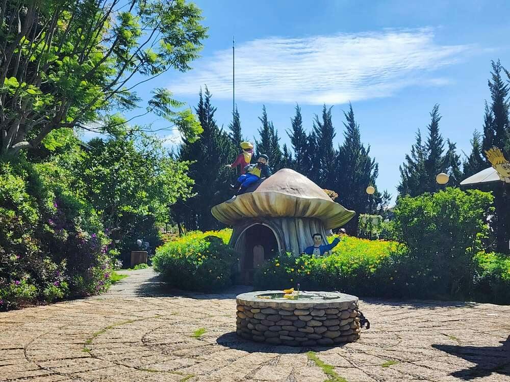 A whimsical garden scene featuring a large mushroom-shaped structure with colorful statues and a stone well in the foreground.