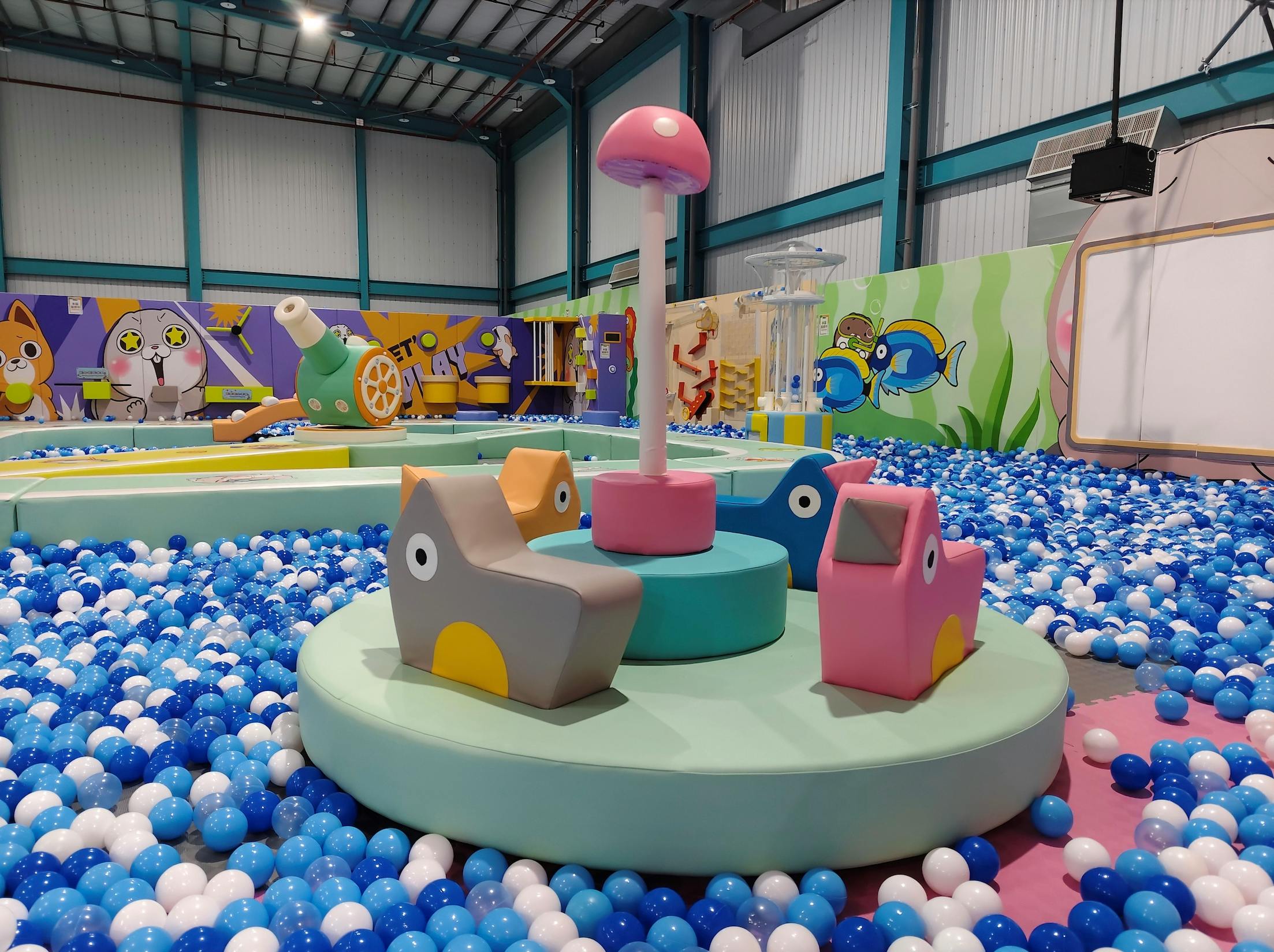 Indoor playground with a colorful rotating platform surrounded by a blue and white ball pit, featuring animal-shaped seats.
