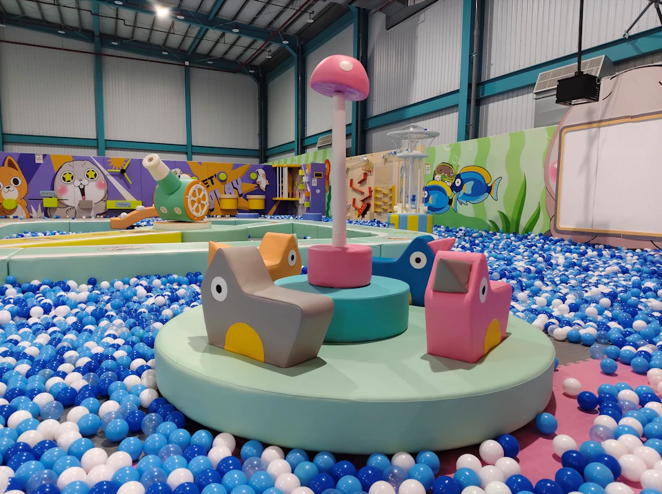 Indoor children's play area with colorful soft structures, a ball pit, and decorative cartoon-themed walls.