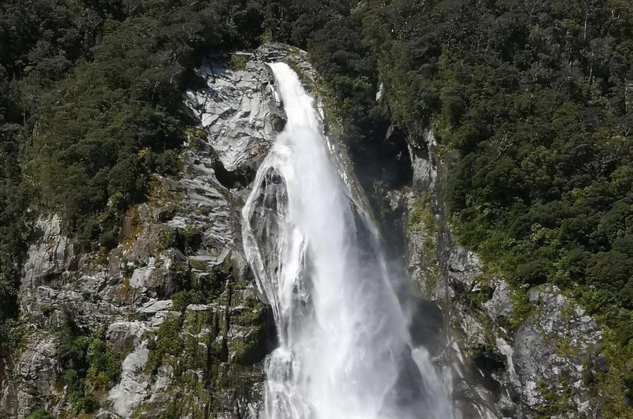 A tall waterfall cascading down a rocky cliff surrounded by dense green forest.