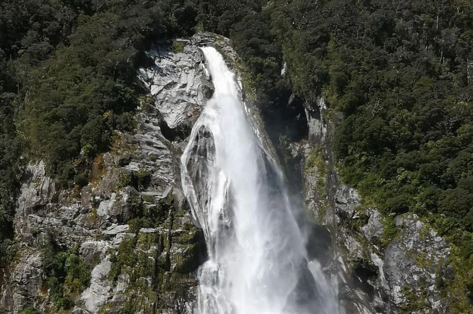 A tall waterfall cascading down a rocky cliff surrounded by dense green forest.