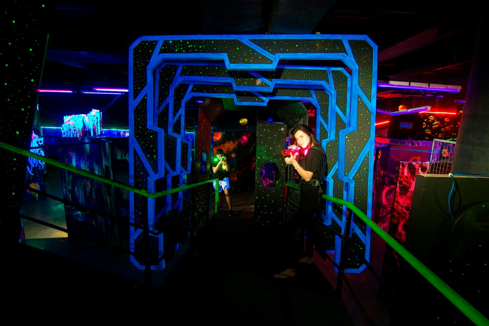 People playing laser tag in a dimly lit arena with neon decorations and glowing laser guns.