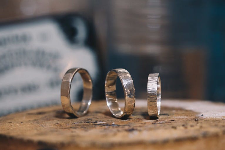 Three silver rings with various textures are arranged upright on a wooden surface with a blurred background.
