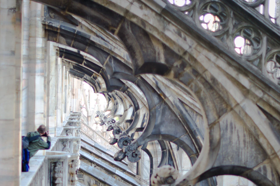 Gothic stone arches and ornate carvings on the side of a historic building, featuring intricate details and pointed structures.