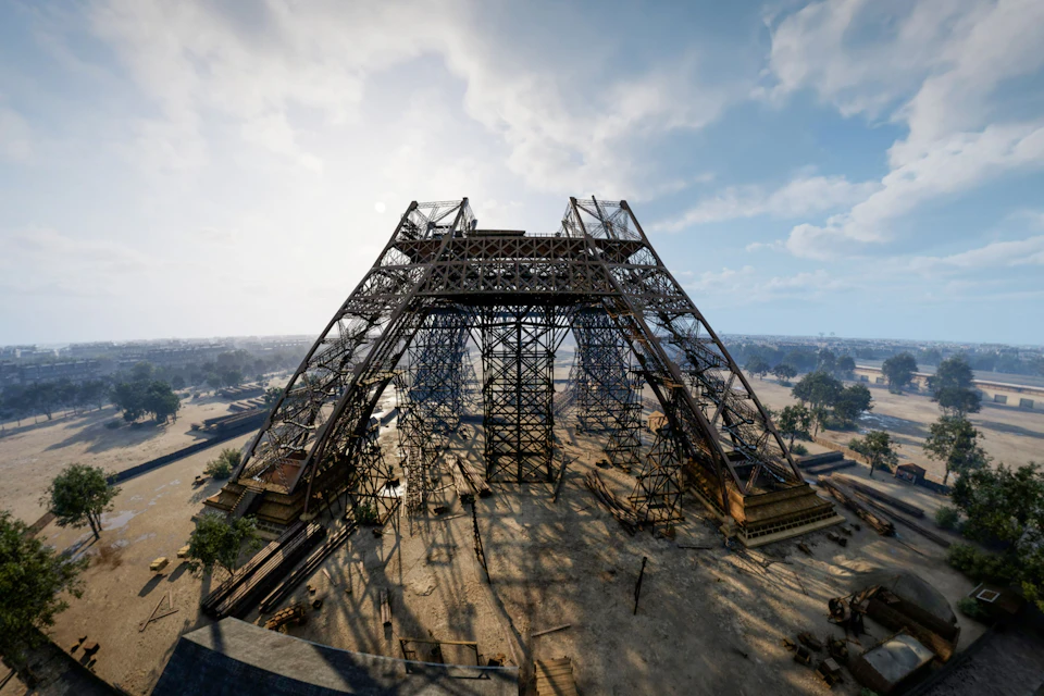 A large metal framework structure under construction in an open area, with a clear sky and scattered vegetation around.