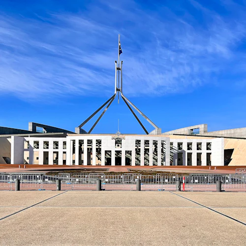 Modern regeringsbyggnad med en hög flaggstång och en bred innergård under en klarblå himmel.
