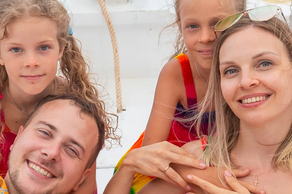 A family of four relaxes on a boat with bean bags, surrounded by water and green hills in the background.