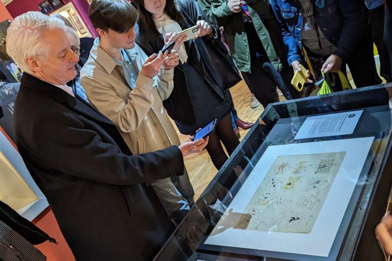 Un gruppo di persone che osserva una vetrina in un museo o in un'esposizione, con alcuni che scattano foto dell'esposizione.