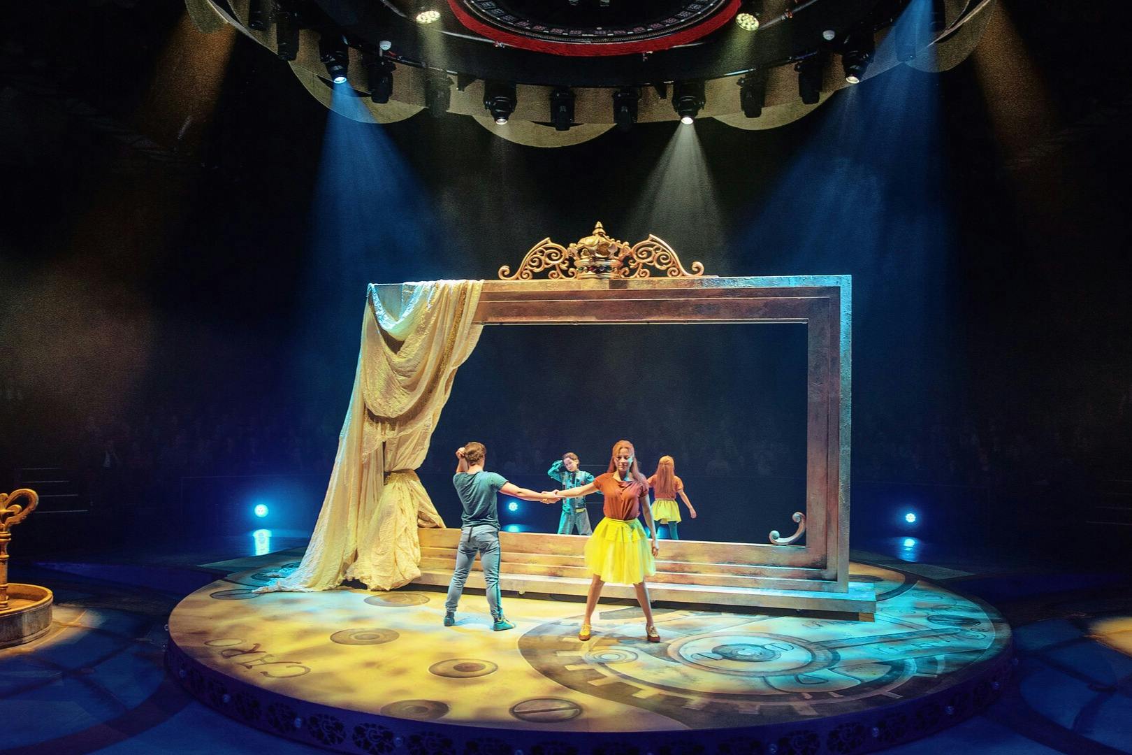 Performers on a stage with elaborate lighting, featuring a large decorative frame and drapes. A singer stands in the foreground.