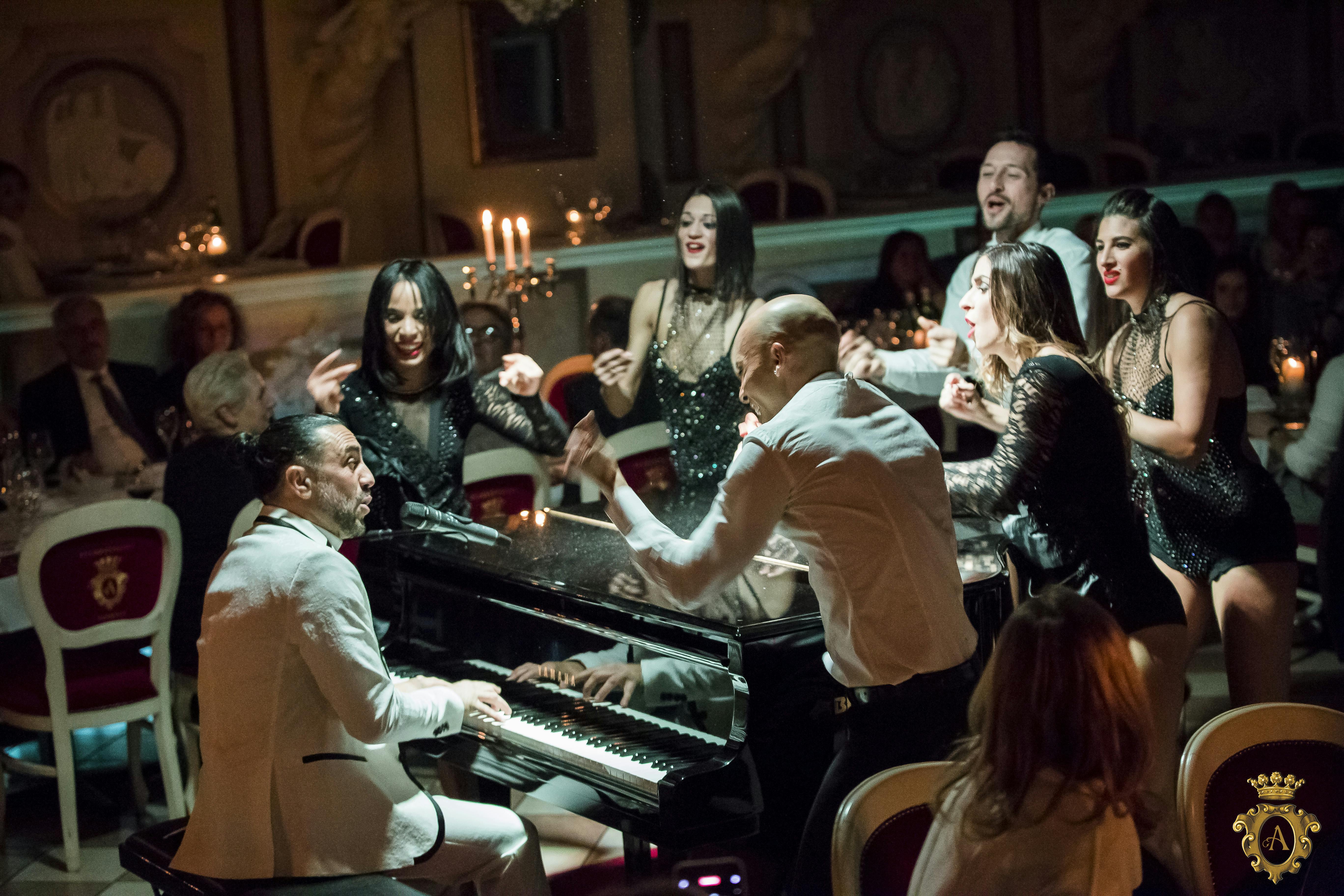 一位男士弹钢琴，周围的人在昏暗优雅的环境中唱歌跳舞，烛台和坐着的房客坐在一起。