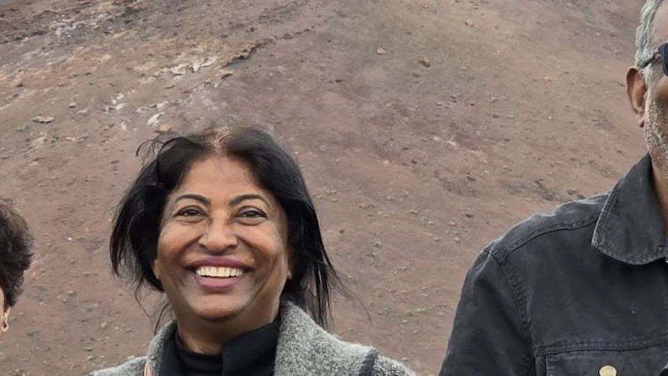 Three people smiling in front of a rocky, mountainous landscape with mist, under an overcast sky.