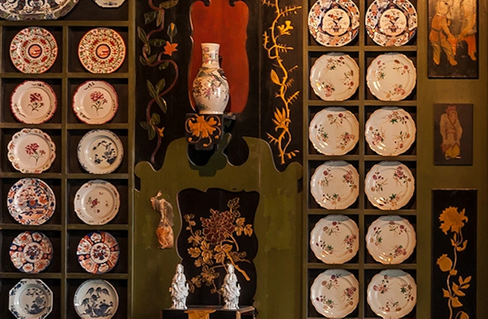 Ornate room with decorative wall plates, dark wooden furniture, patterned carpet, and intricate wall art featuring dragons and floral motifs.