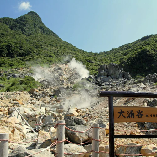 A scenic view of a steaming rocky valley with green mountains in the background and a wooden sign in the foreground.