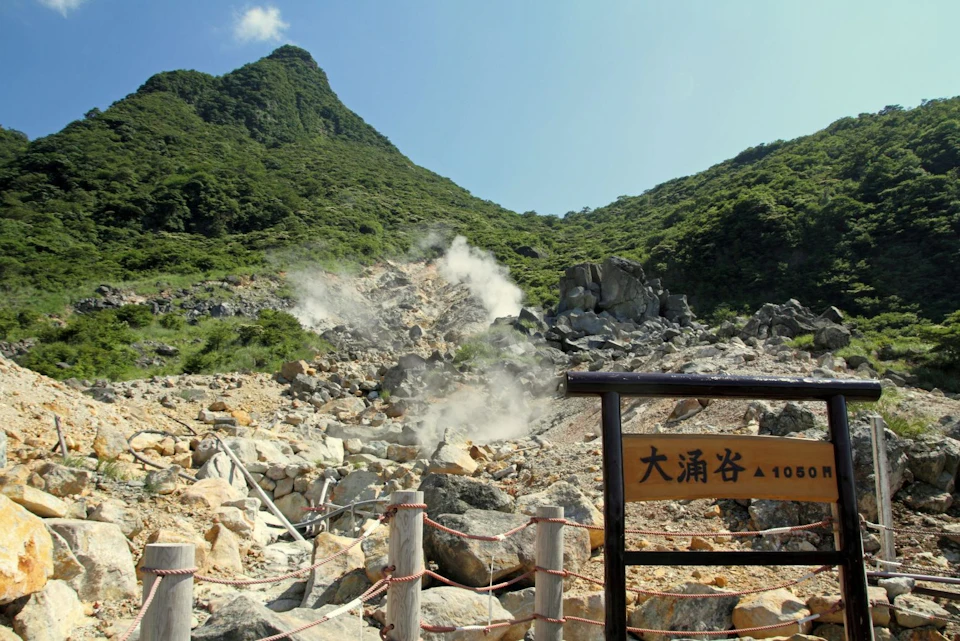 A scenic view of a steaming rocky valley with green mountains in the background and a wooden sign in the foreground.
