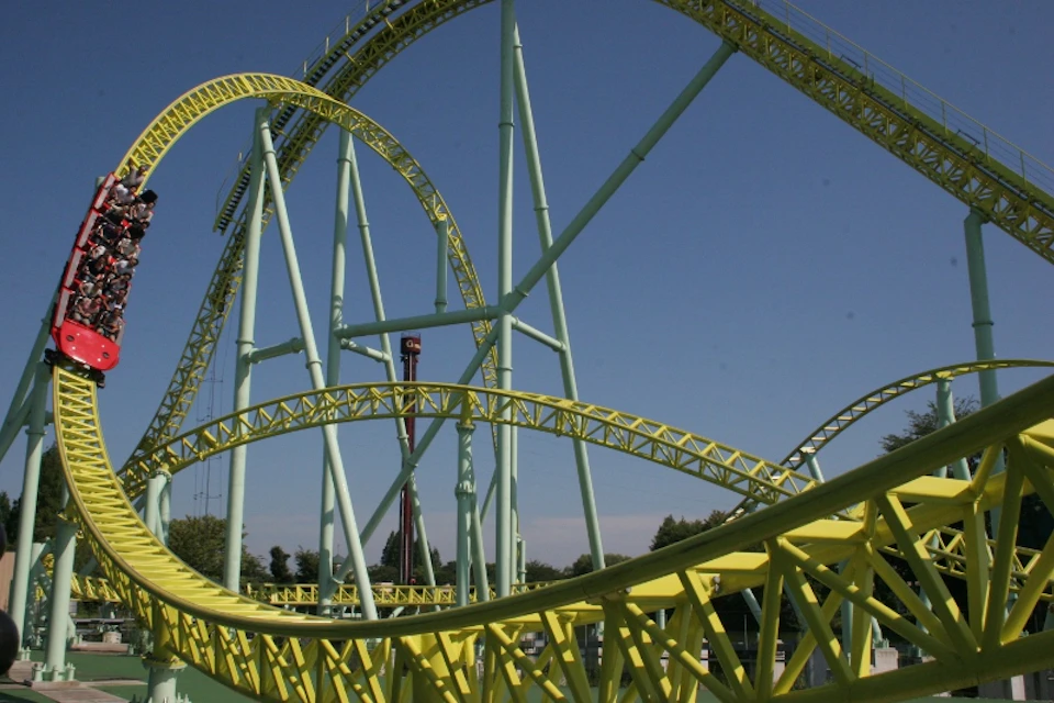A green and yellow rollercoaster with looping tracks under a clear blue sky.