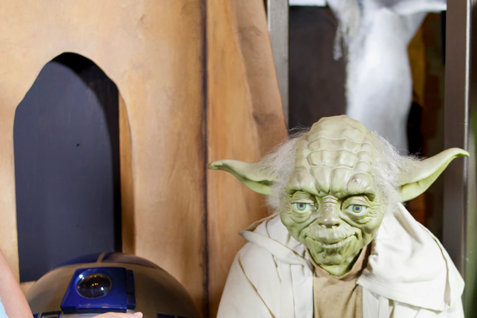 Three girls smiling and posing with statues of Yoda and R2-D2 inside a themed exhibit.