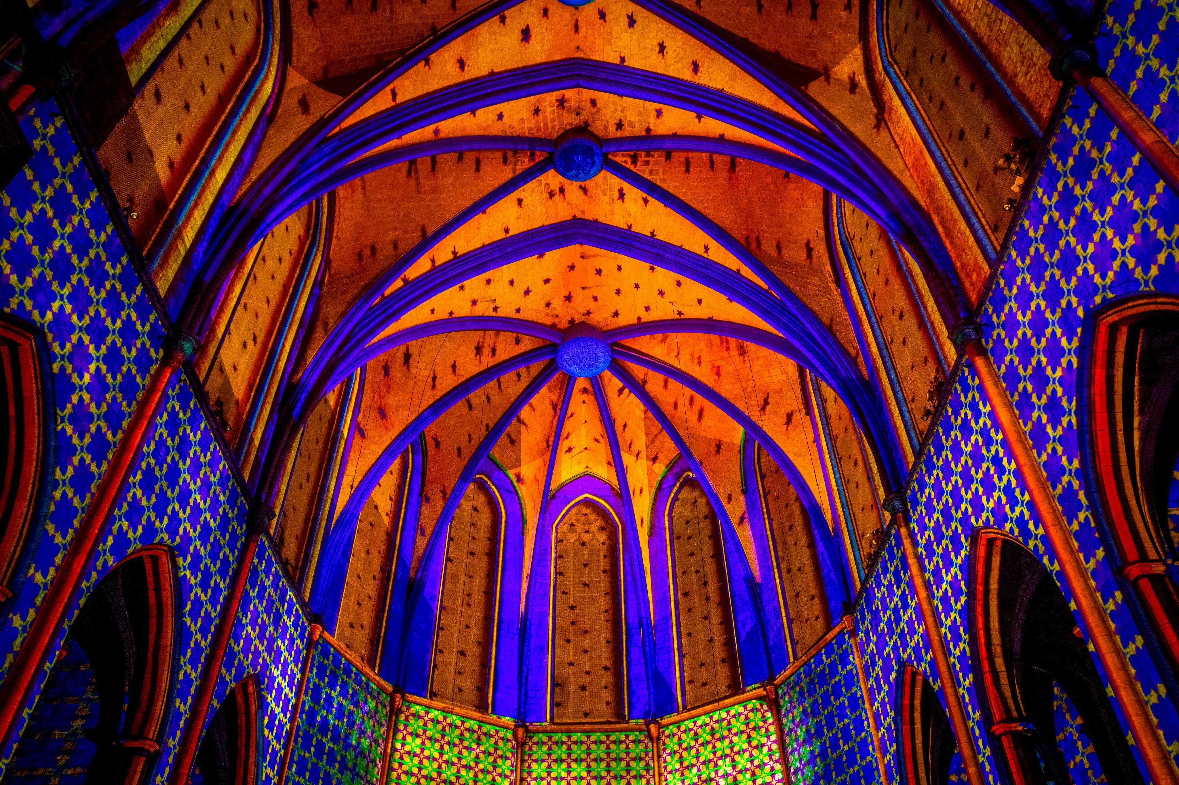 Plafond voûté coloré de style gothique avec des motifs bleu, orange et vert vibrants et des dessins complexes.