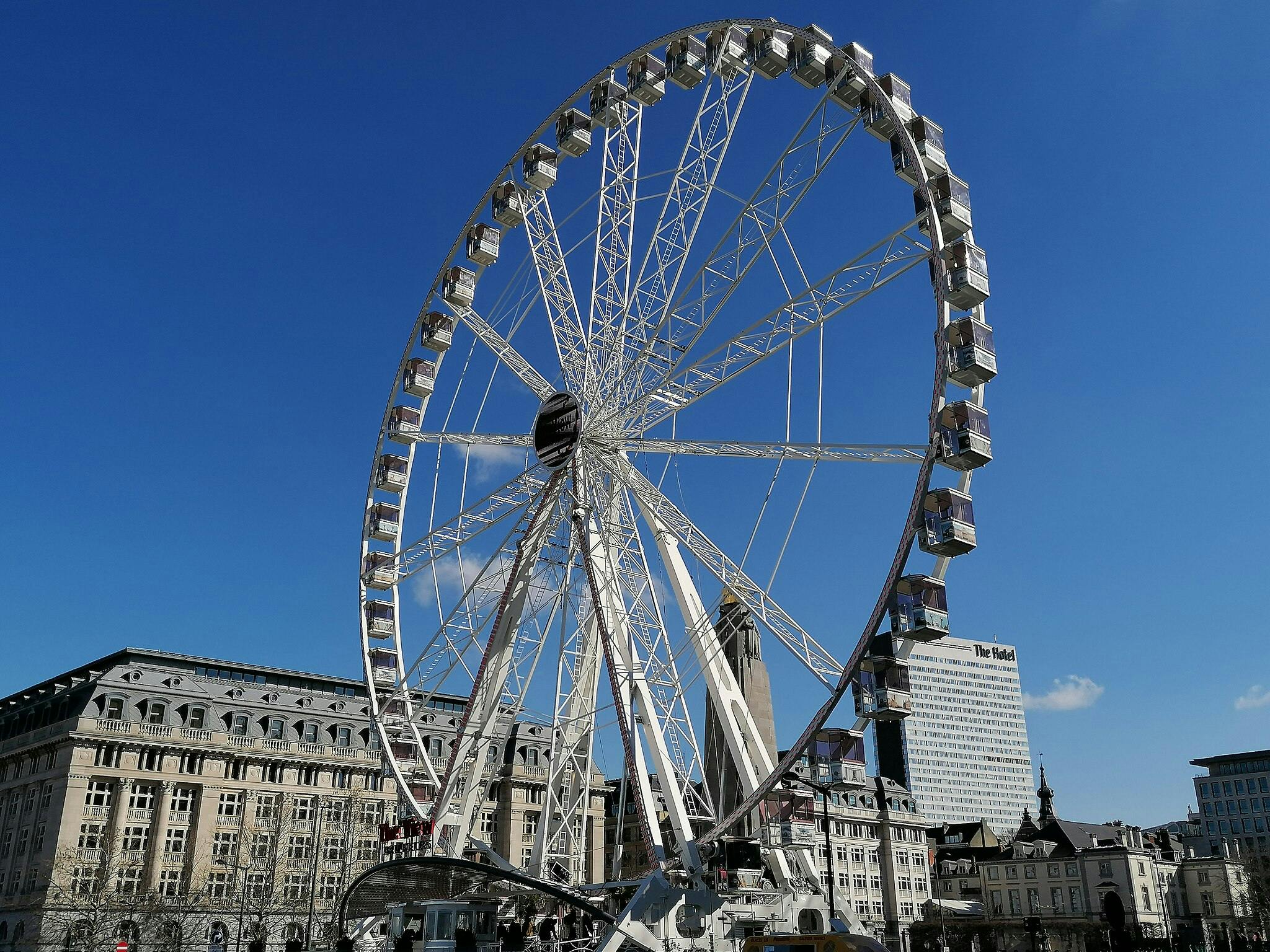 Une grande roue devant des bâtiments historiques et modernes sous un ciel bleu clair.