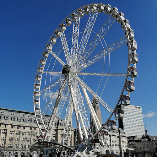 Ett stort pariserhjul framför historiska och moderna byggnader under en klarblå himmel.
