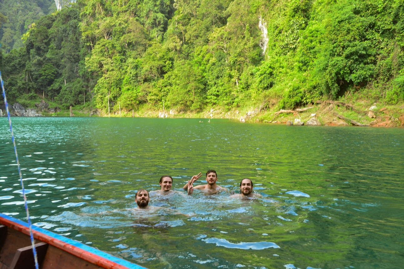 四个人在郁郁葱葱的绿树和悬崖环绕的湖中游泳。