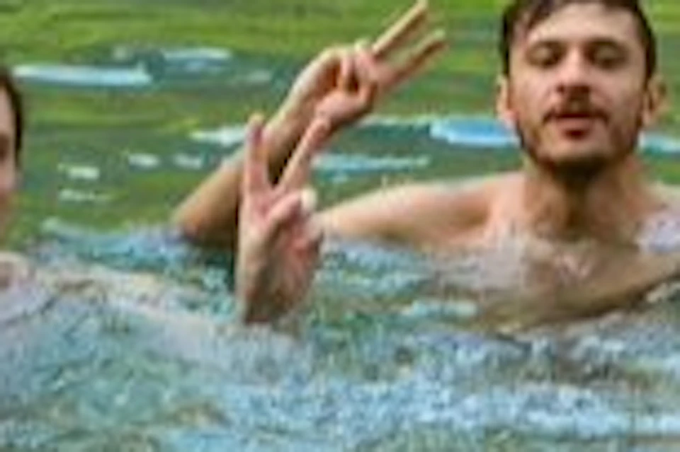 Four people swimming in a lake surrounded by lush green trees and cliffs.