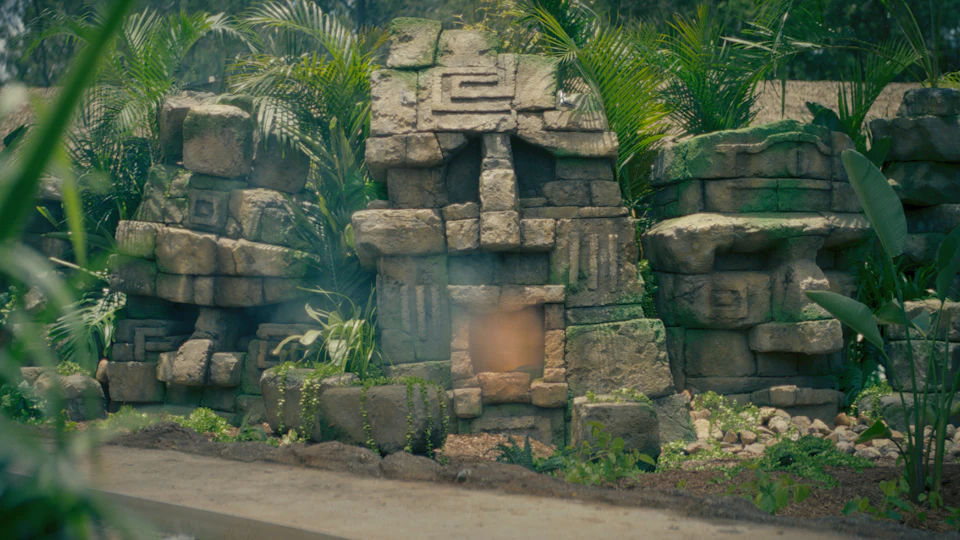 A stone structure resembling a face, surrounded by green foliage.