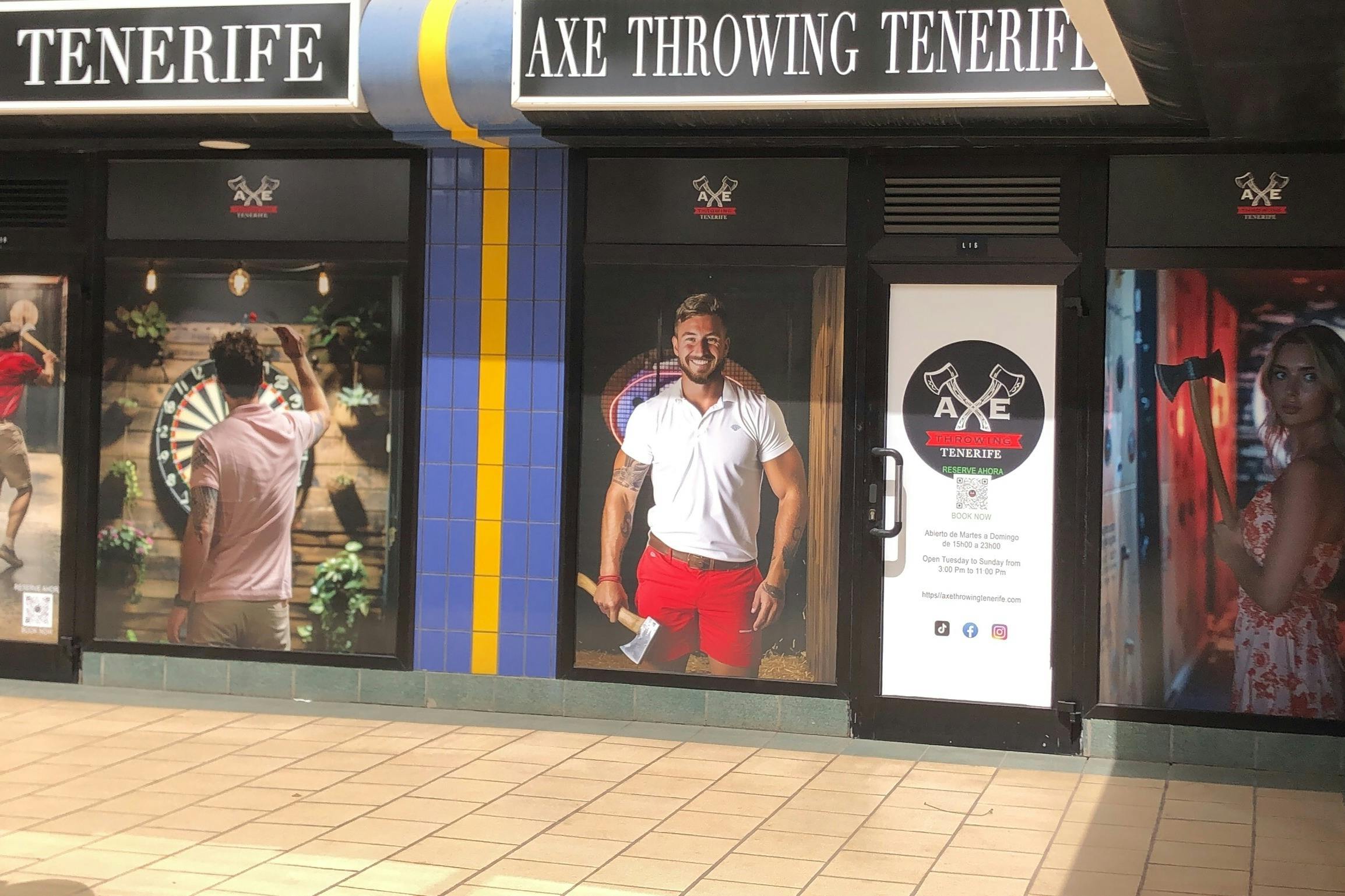 Aparador amb grans finestrals on es mostren imatges promocionals de “Axe Throwing Tenerife”. Les persones es representen sostenint eixos i apuntant dards.