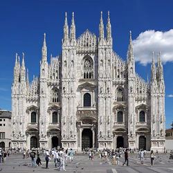 Grandeur-katedralen med invecklade spiror och flera dörröppningar, med många människor på ett torg under en klarblå himmel.