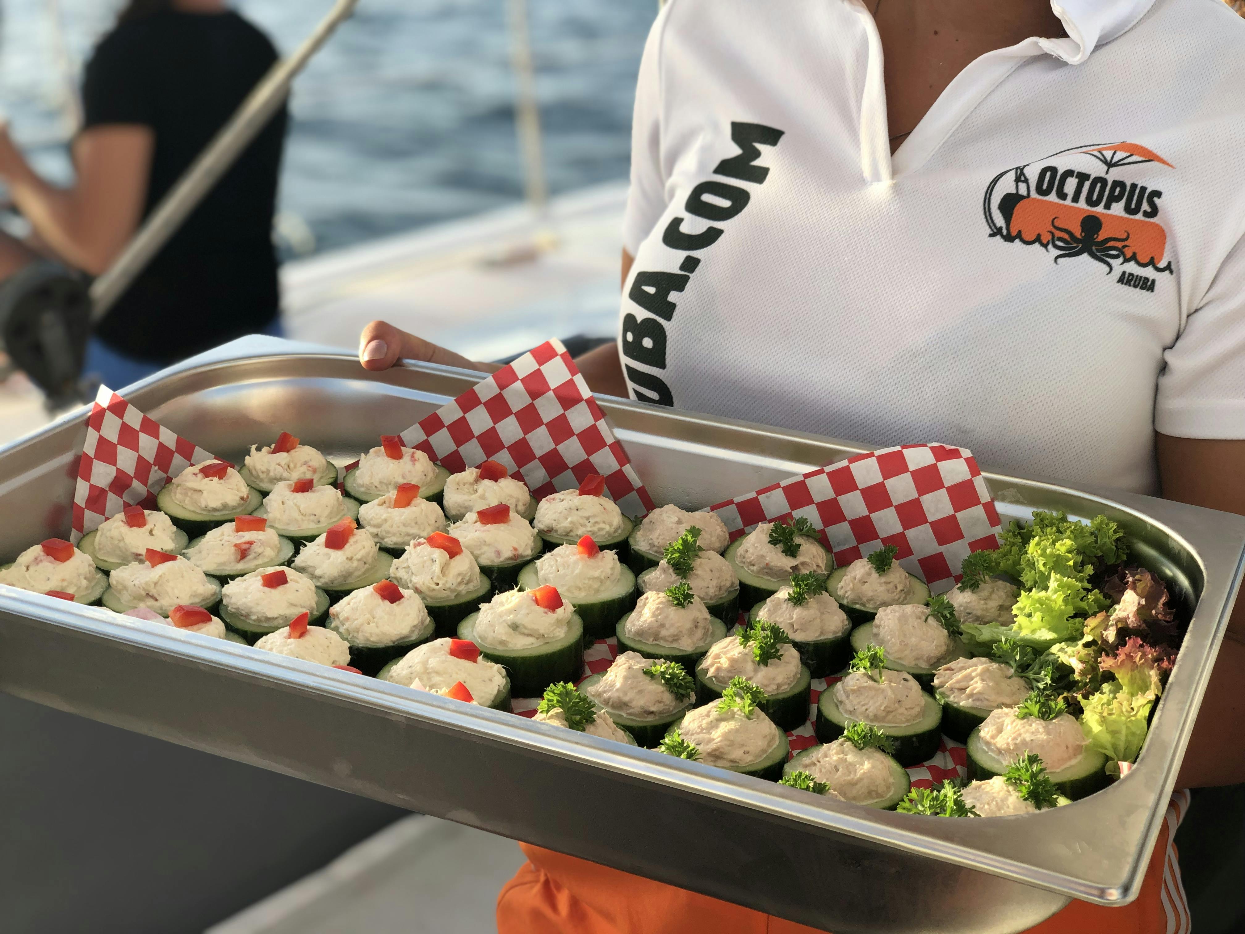 A person holds a tray with stuffed cucumber appetizers, garnished with herbs, and checkered paper over a boat deck near water.