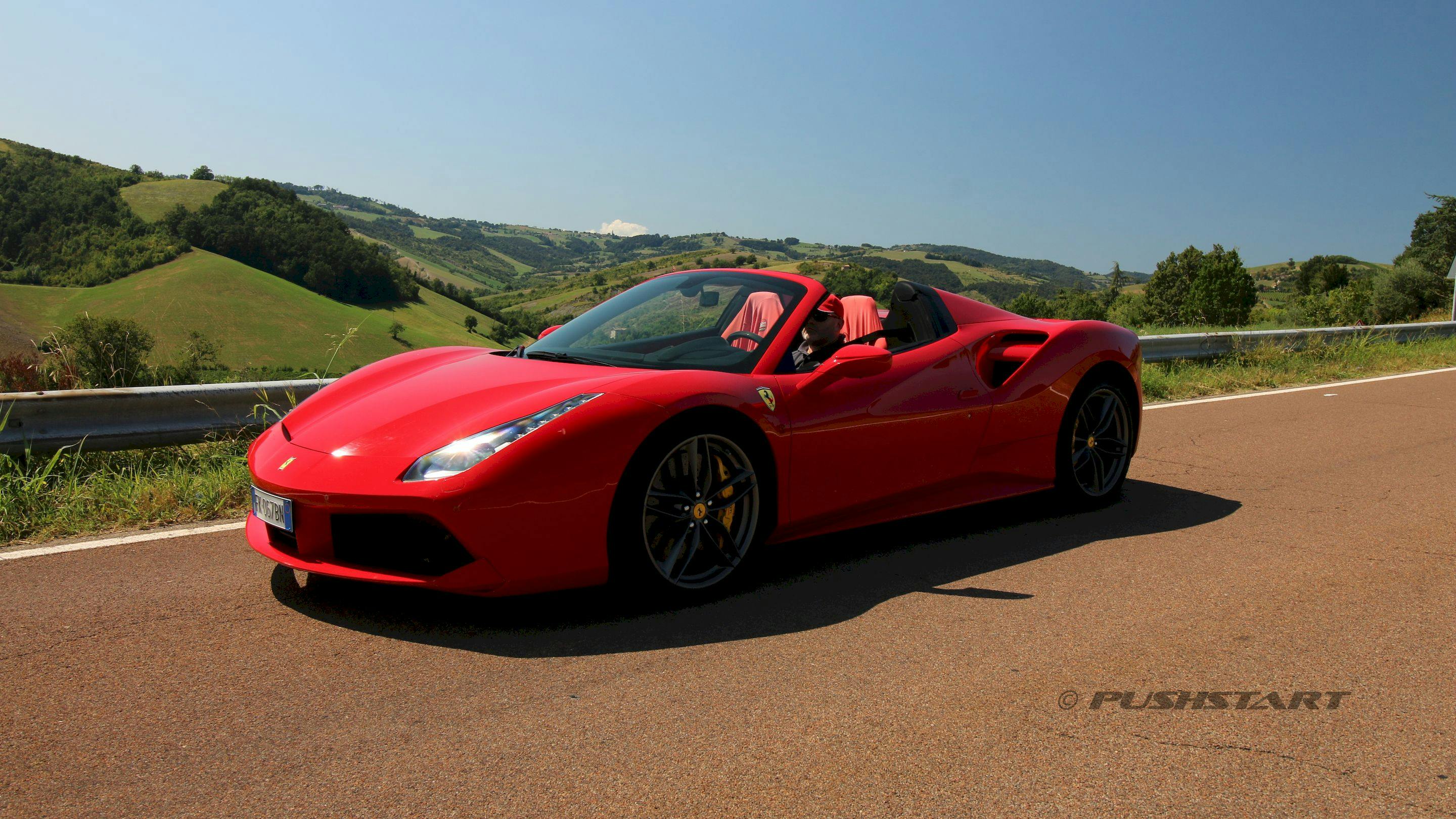 A red convertible sports car parked on a country road with scenic green hills in the background.