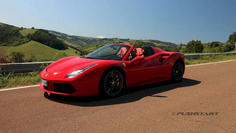A red convertible sports car parked on a country road with scenic green hills in the background.