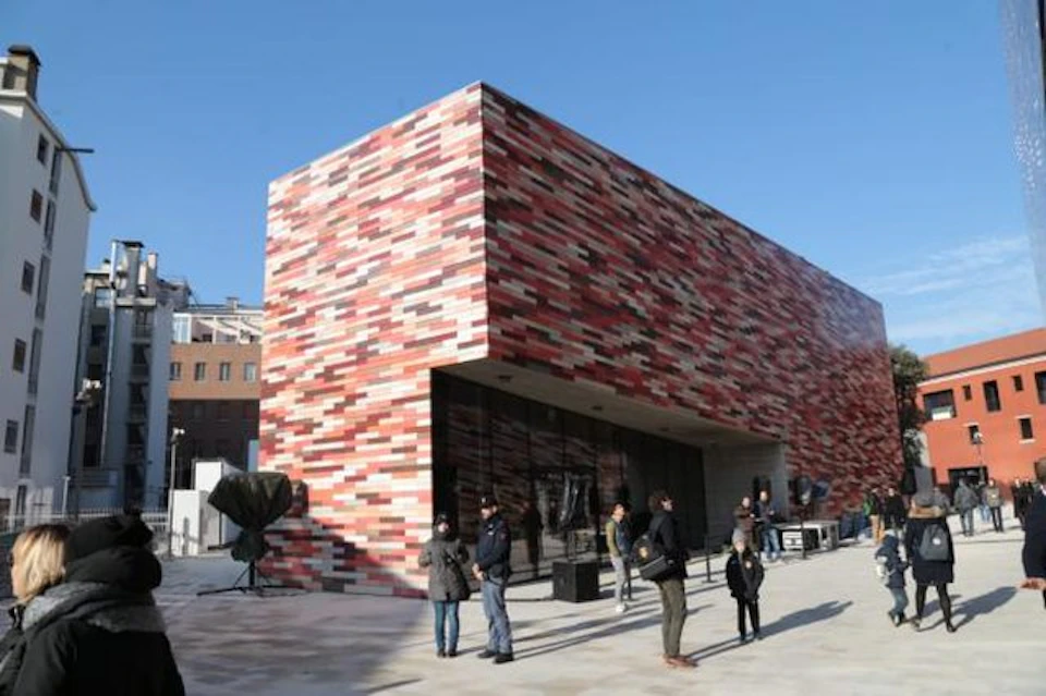 People standing near a modern red and pink patterned brick building on a clear day.