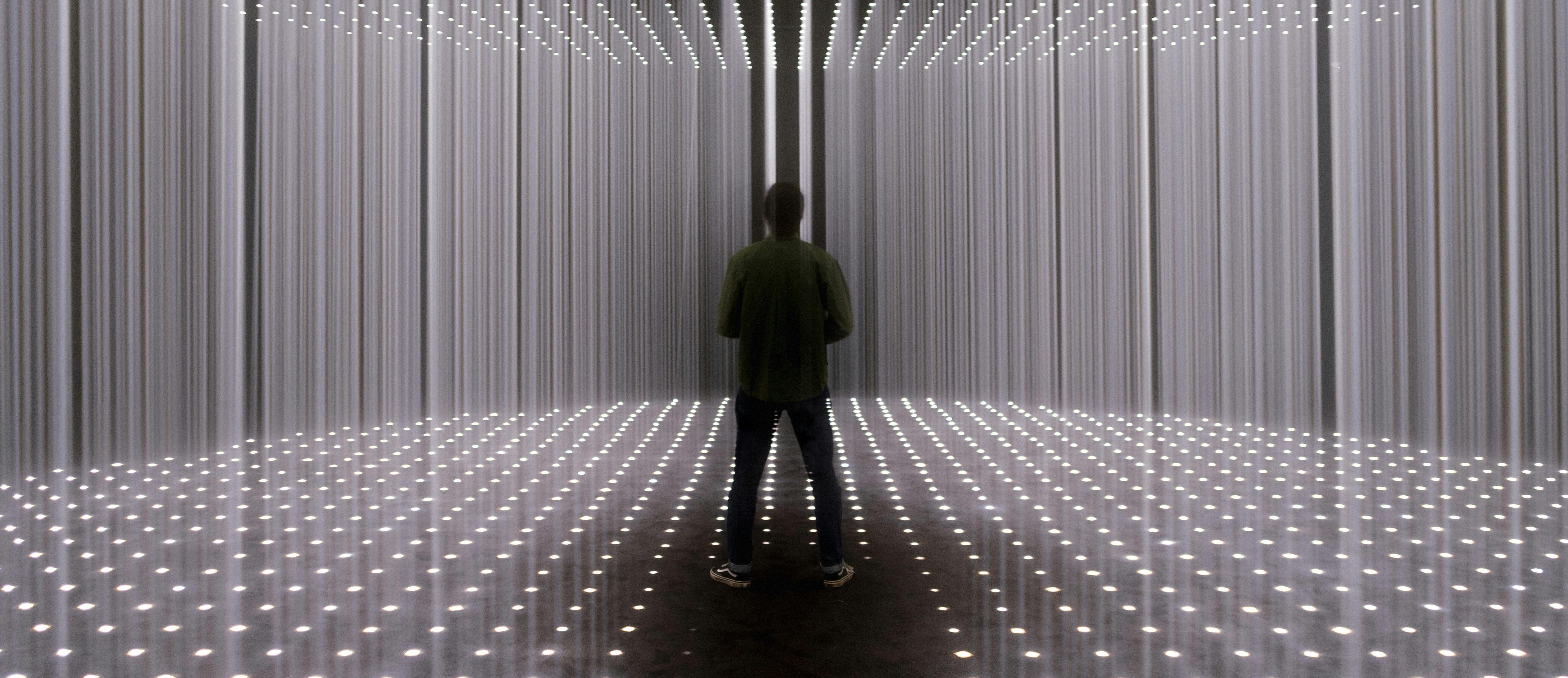 一个人站在一个房间里，墙壁和天花板上有垂直的灯条，地板上有小而均匀的灯光。