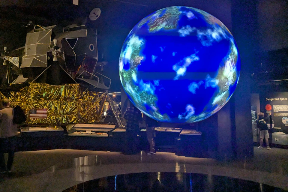 A glowing Earth model and a spacecraft exhibit displayed in a dimly lit science museum setting.