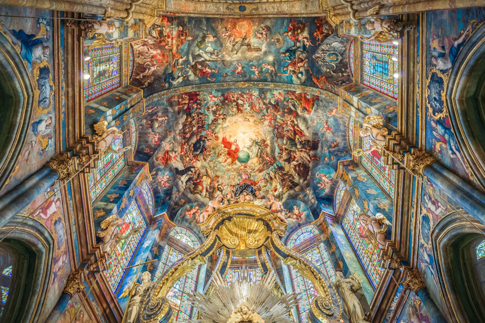 Ornate church ceiling adorned with detailed frescoes depicting a heavenly scene, surrounded by colorful stained glass windows.