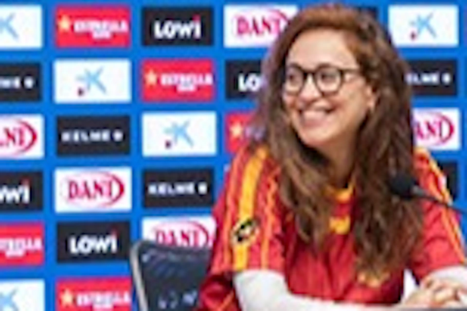 Three people seated at a press conference table in front of a backdrop with logos, in a room with a wood-paneled wall.