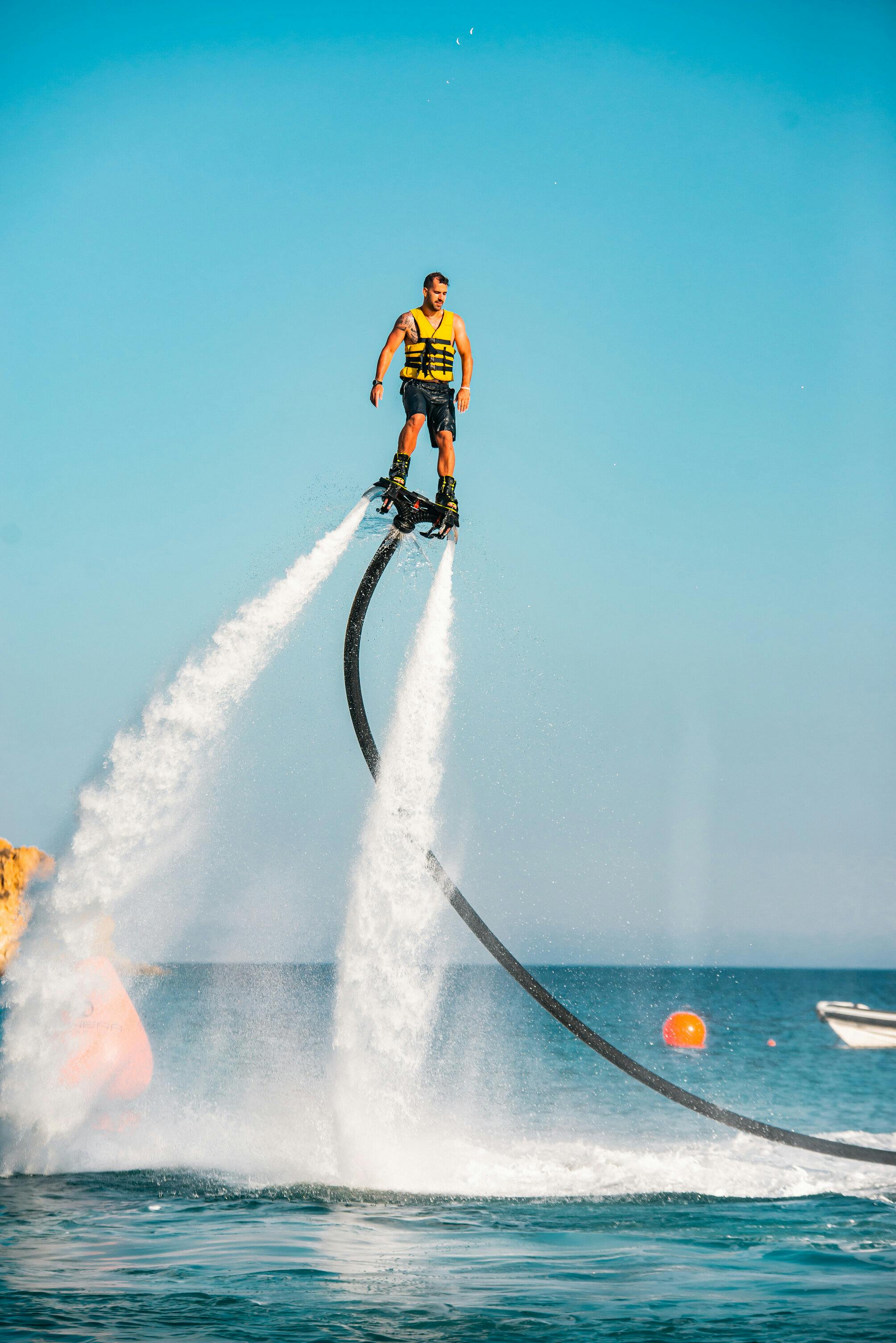 바다 위를 날아다니는 노란색 구명 조끼를 입은 사람이 워터젯을 타고 위로 올라가고 배경은 맑고 푸른 하늘입니다.