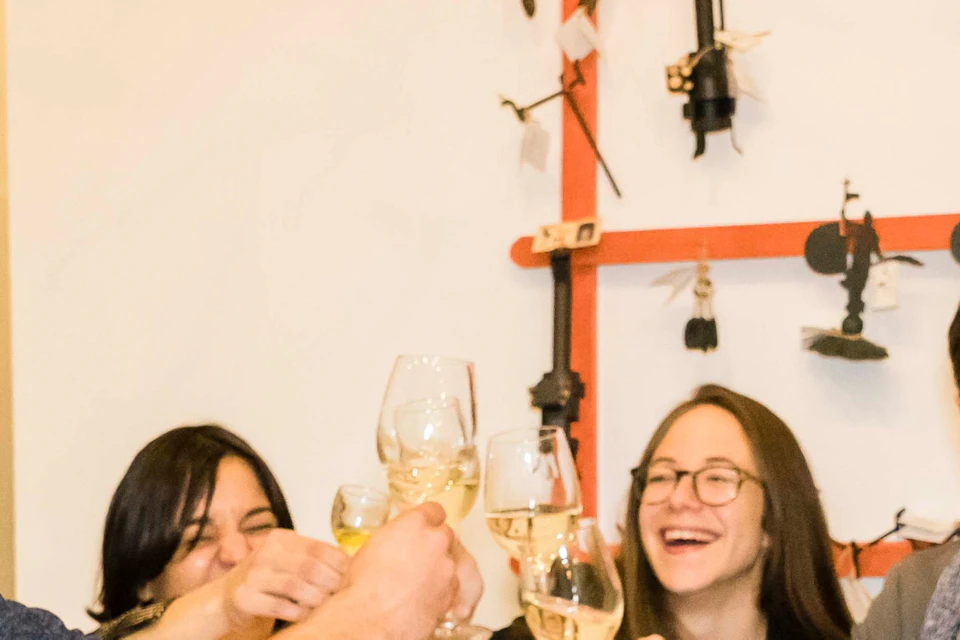 Four people laughing and clinking wine glasses around a table with food and drinks.