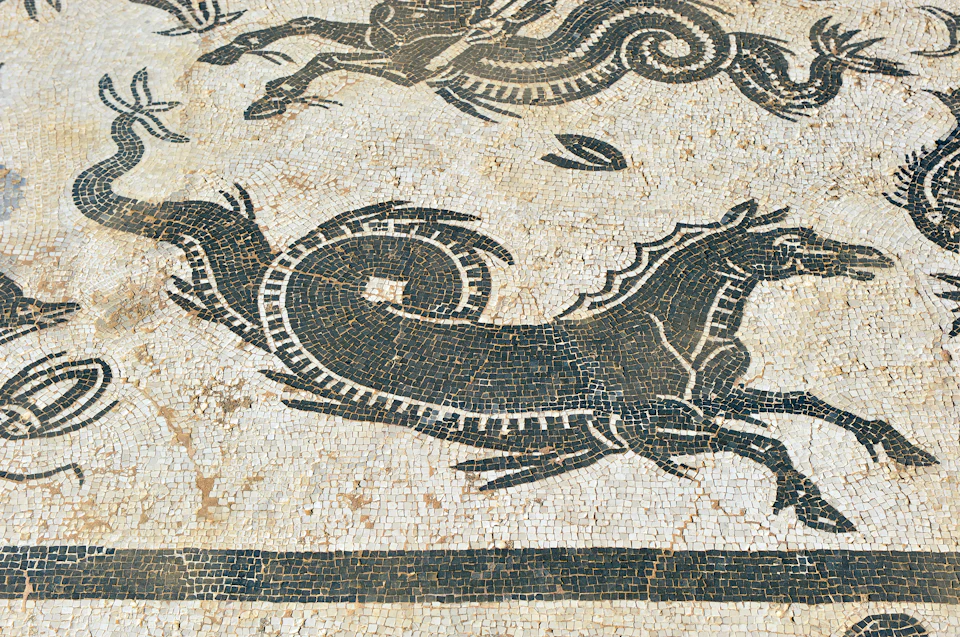 Ancient mosaic featuring a black, stylized horse and serpent-like creatures against a white and beige background.
