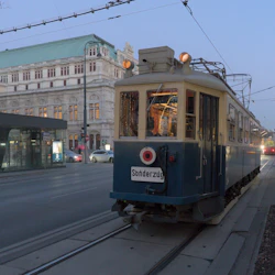 En vintage spårvagn märkt "Sonderzug" på stadsspår. En historisk byggnad med grönt tak ligger i bakgrunden.
