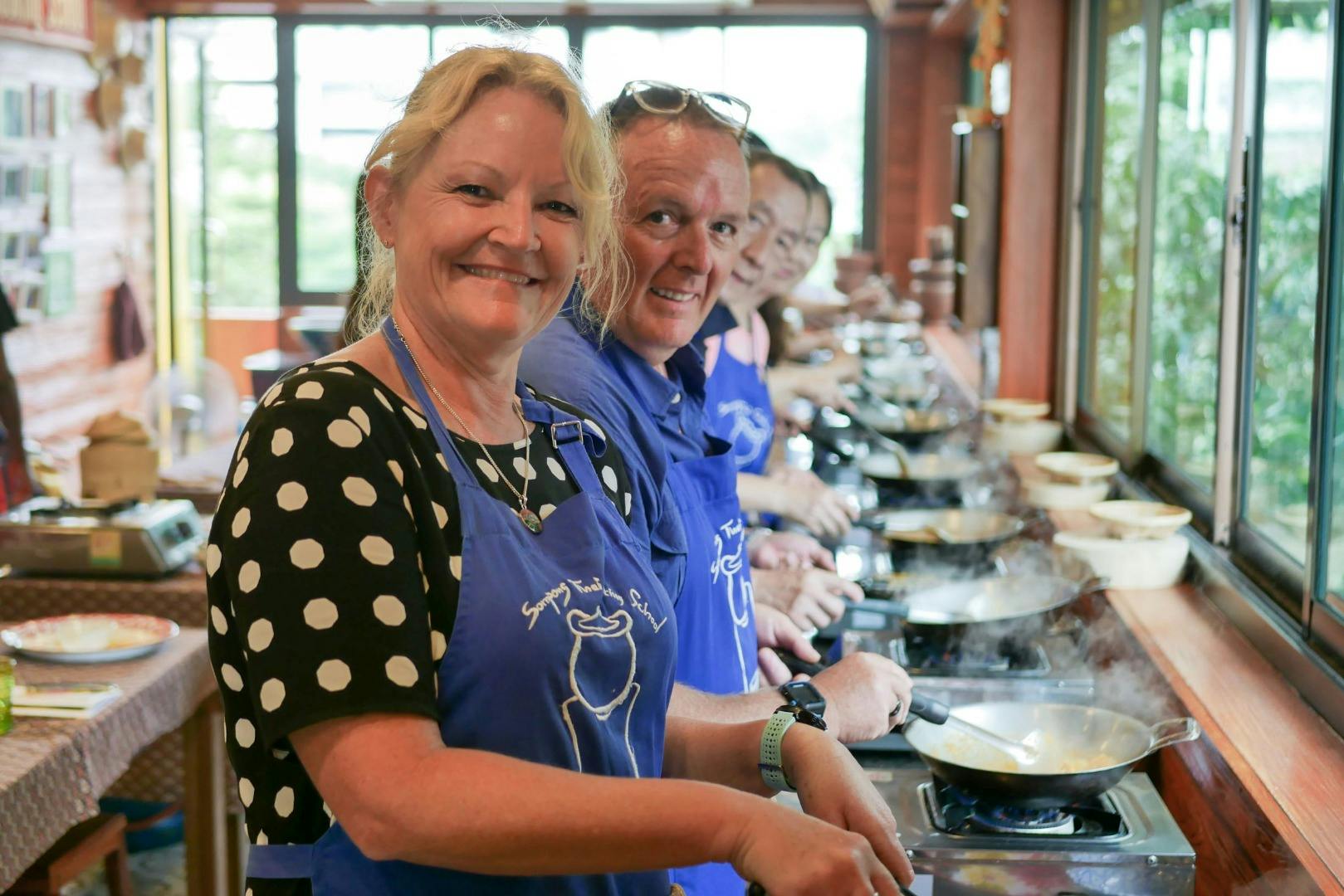 People wearing aprons and smiling while cooking at a culinary class in a bright kitchen.