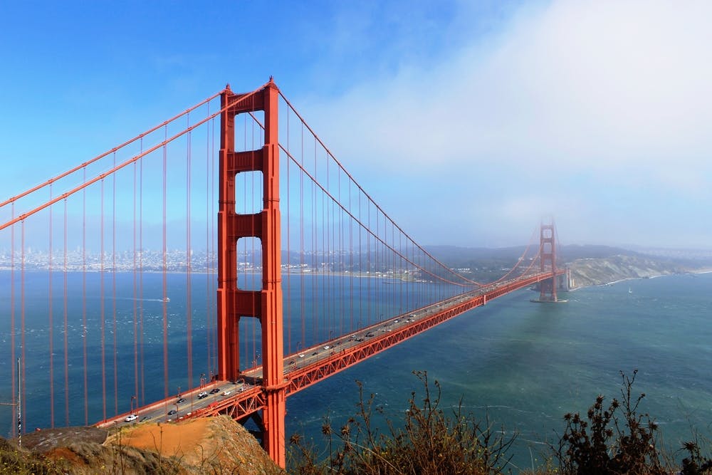 这张照片显示金门大桥横跨水面，将晴朗的蓝天下的陆地地区与一些遥远的雾联系起来。