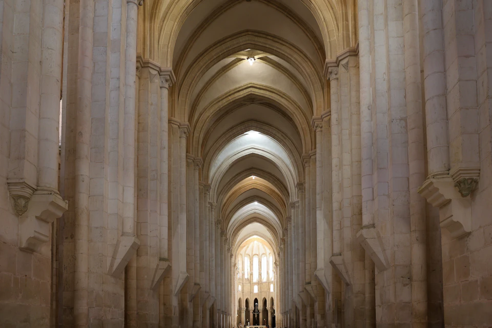Interior view of a cathedral with tall, pointed arches and bright light streaming through windows at the far end.