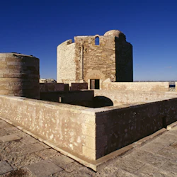 Forntida stenfästning med runda torn och välvda dörröppningar under en klarblå himmel.