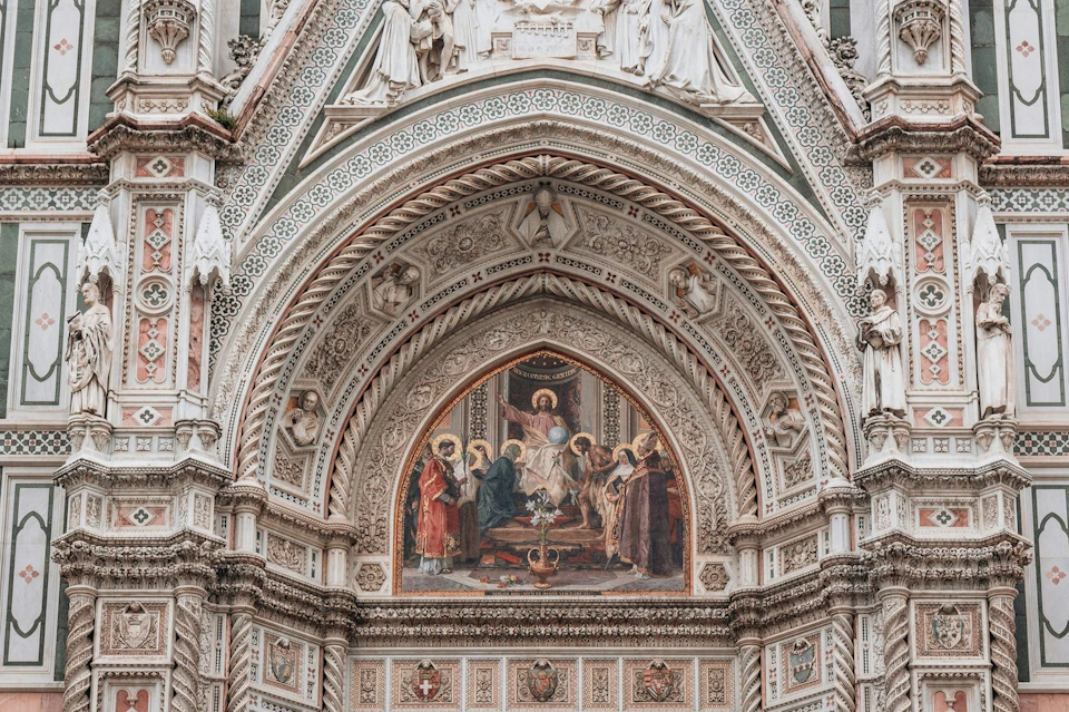 Ornate architectural detail with an intricate fresco depicting religious figures and elaborate carvings under a gothic arch.