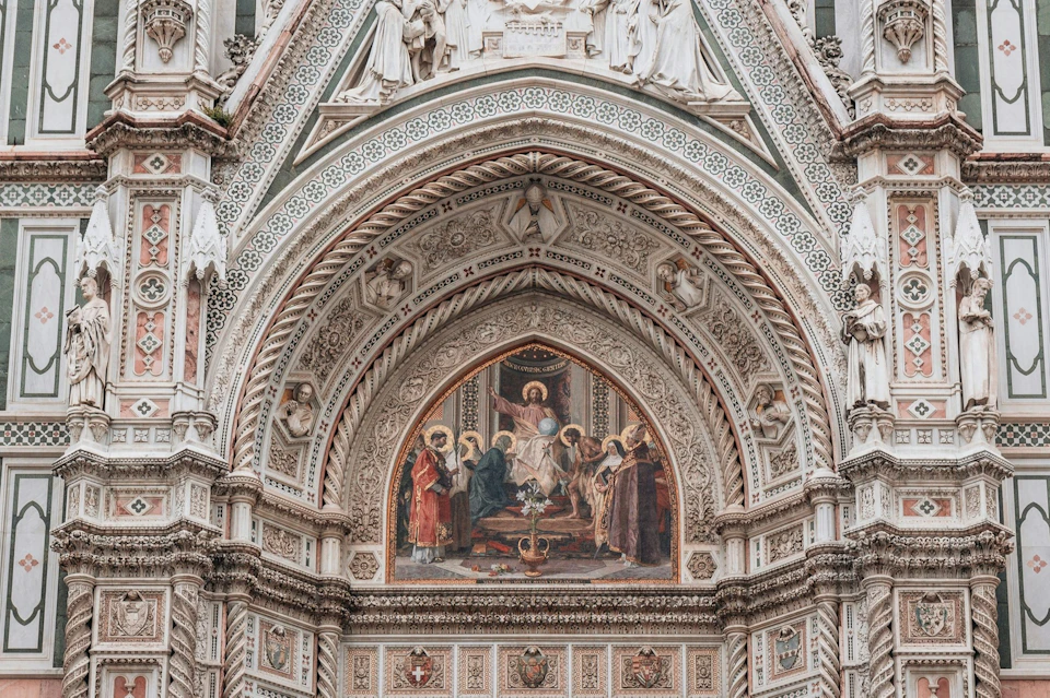 Ornate architectural detail with an intricate fresco depicting religious figures and elaborate carvings under a gothic arch.